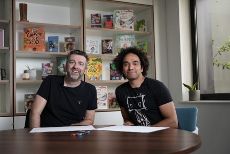 two men smiling and sitting at table with white paper and crayons